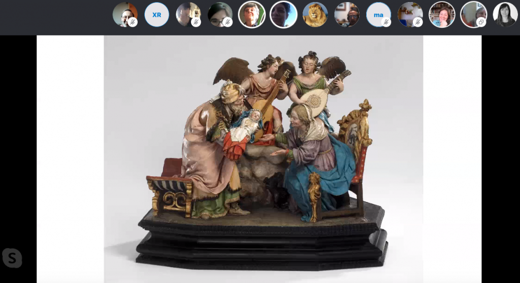 Captura de pantalla de la aplicación skype. En la franja superior se ven 13 imágenes en miniatura de las personas participantes, debajo la terracota de Luisa Roldán de La Virgen Niña con San Joaquín y Santa Ana.