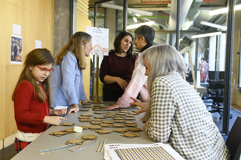 Imagen del taller Touch Emoji en Medialab. Una mujer y una niña conversando sobre los emojis ante una mesa. Al fondo otras tres mujeres de pie hablando. 