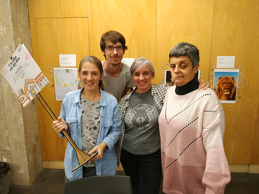 Cuatro integrantes del equipo de MiméticasLab mirando a cámara, al fondo se ve la pared con las reproducciones de los cuadros y los emojis en papel pegados junto a ellos.